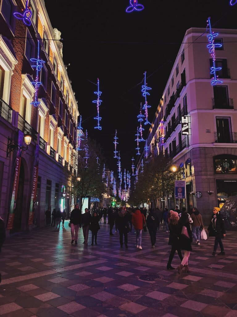 Cobblestone streets of Madrid's historic center lit up at night, with lively groups moving from tapas bars to flamenco venues, illustrating the dynamic nightlife for those considering relocating.