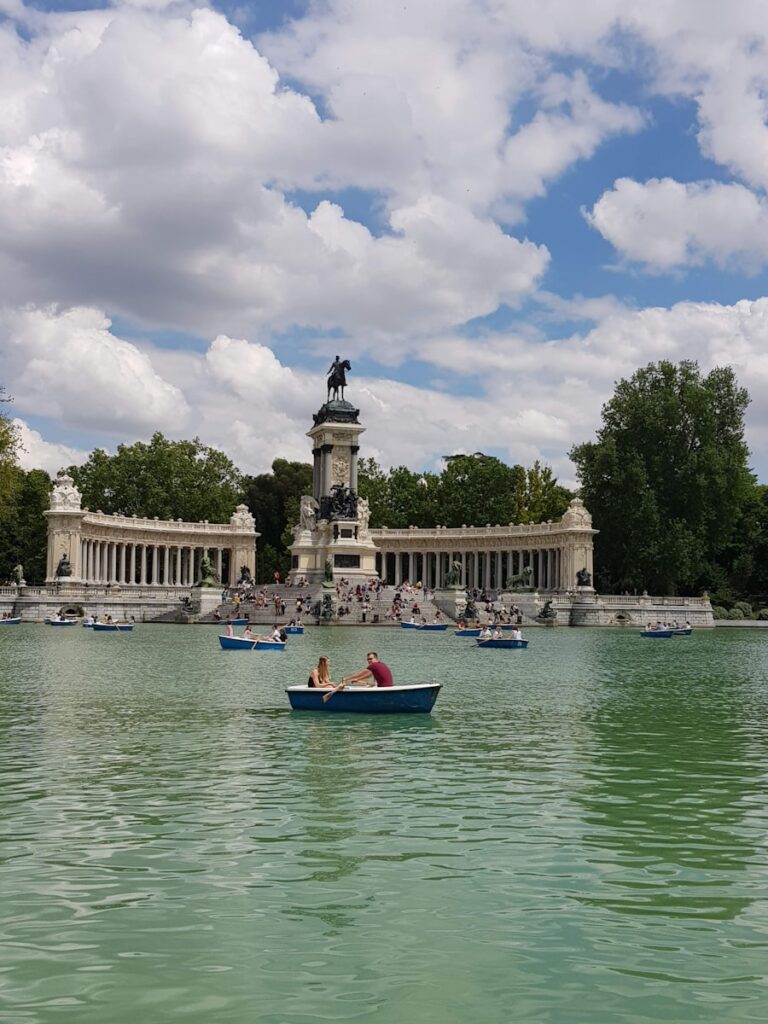 People rowing boats on Retiro Park Lake on a sunny day, showing a fun outdoor activity for those moving to Madrid.